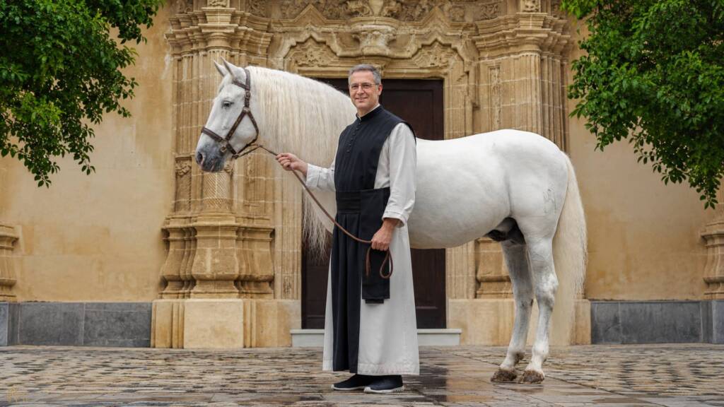 Caballo Cartujano de pura raza española junto a un monje en la Cartuja, frente a una portada monumental.