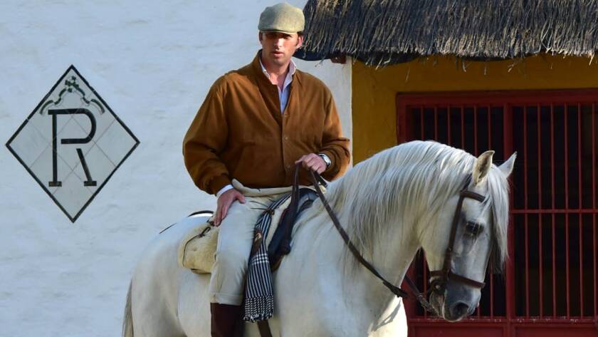 Rafael Peralta Revuelta a caballo junto a una fachada tradicional, montando un caballo PRE blanco.