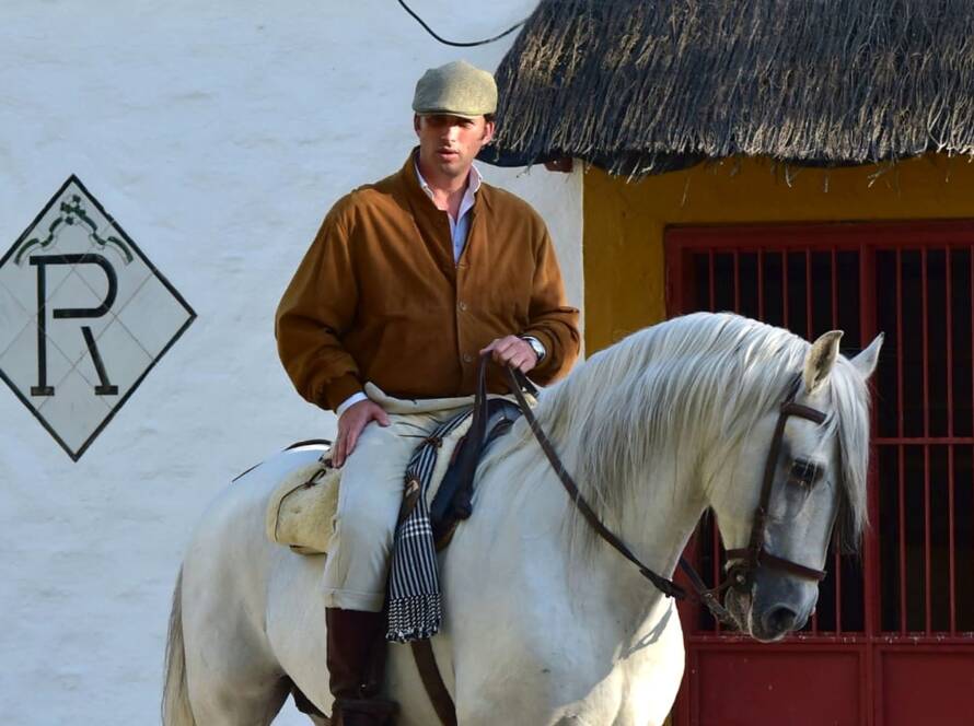 Rafael Peralta Revuelta a caballo junto a una fachada tradicional, montando un caballo PRE blanco.